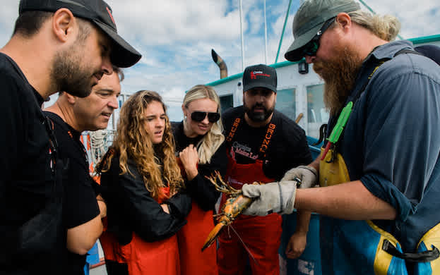 Cousins Maine Lobster franchisees learn about sustainability as a lobsterman shows them a live Maine lobster.