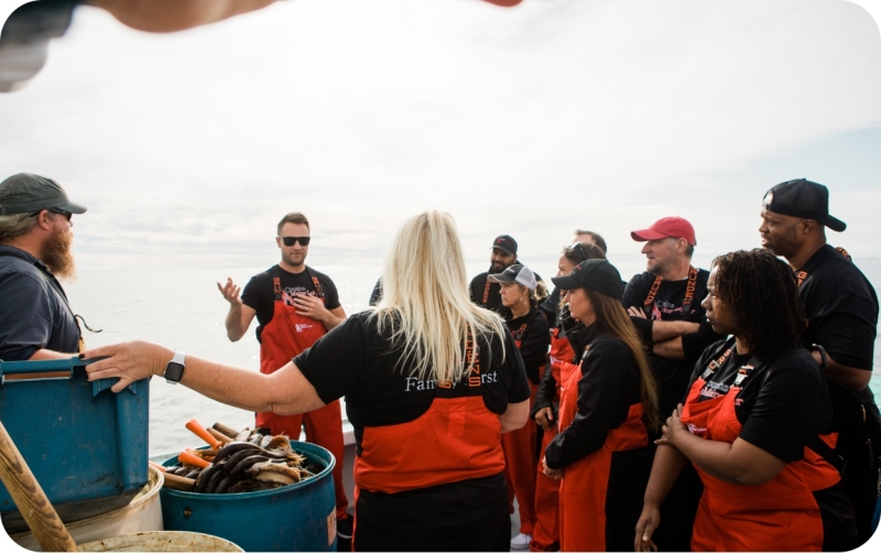 A photo of Cousins Maine Lobster family members on a boat in Maine, listening to Cousin Jim speak as they are out on the water training and fishing.