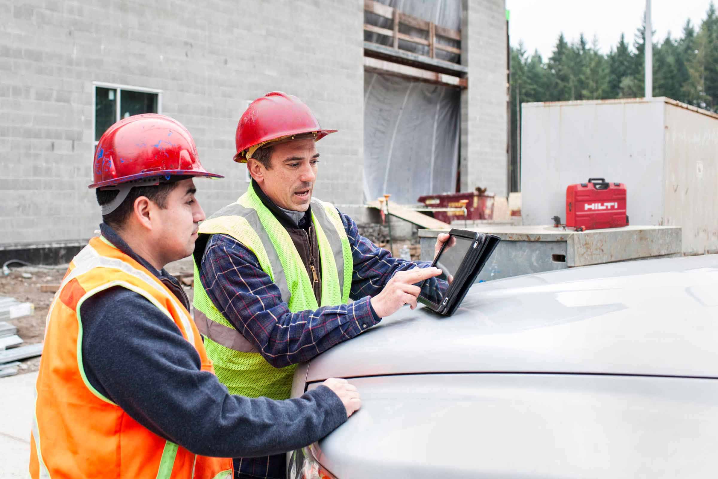 Two construction workers looking at construction software on a tablet on a project jobsite.