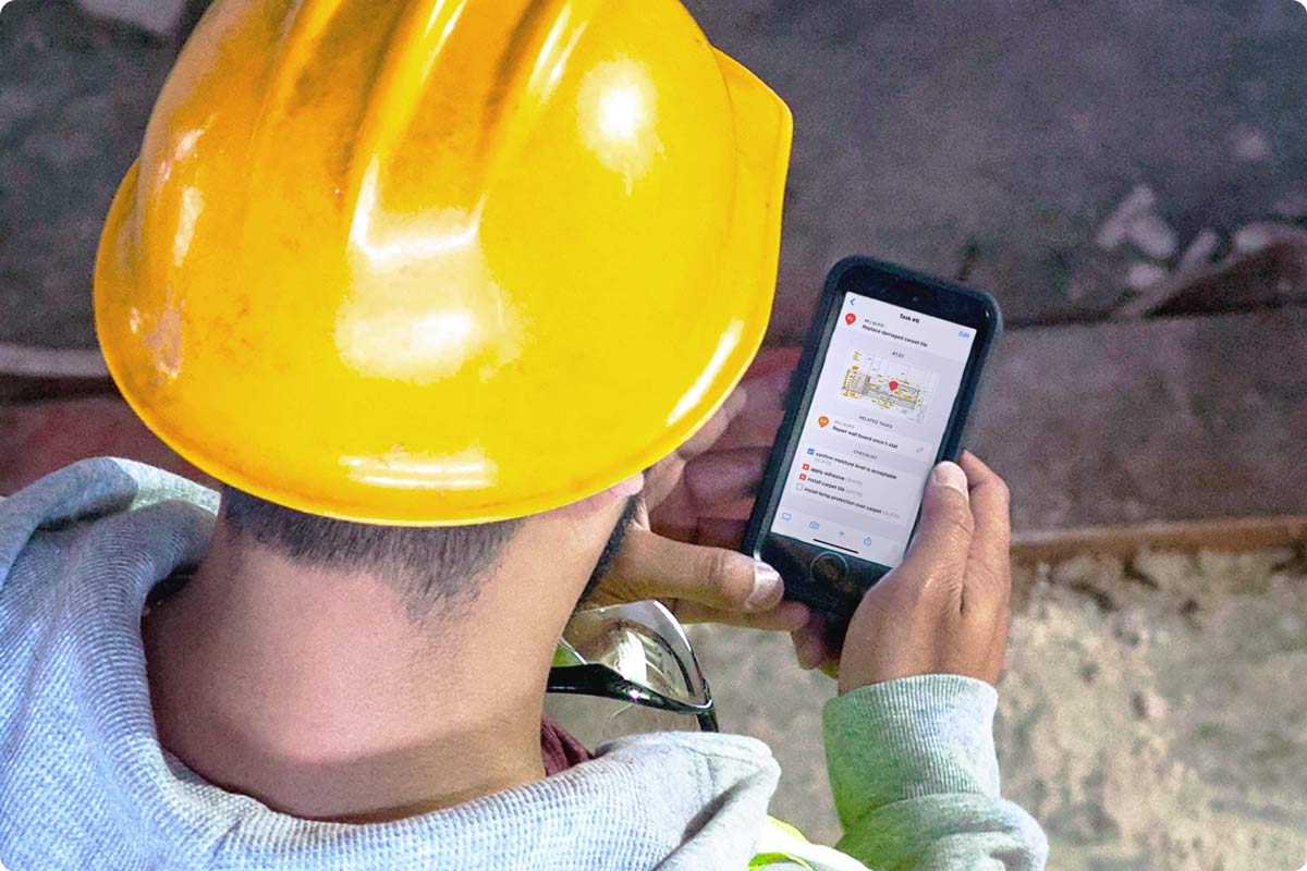 A construction worker is using their iPhone to complete a punch list on the jobsite. They are using Fieldwire to complete it.