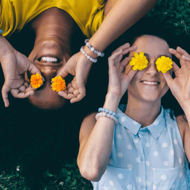 Des jeunes filles sont allongées dans l'herbe et tiennent des fleurs devant leurs yeux