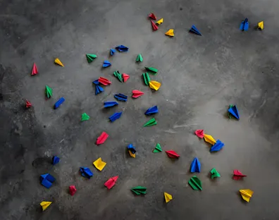 Imagen de un suelo de hormigón sobre el que hay varios aviones de papel, azules, rojos, amarillos y verdes.