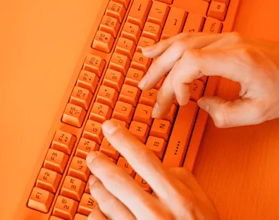 manos escribiendo en un teclado naranja