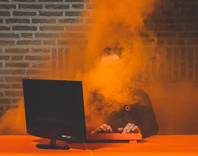 Un hombre con gafas de sol mirando un ordenador sobremesa mientras le envuelve una nube naranja