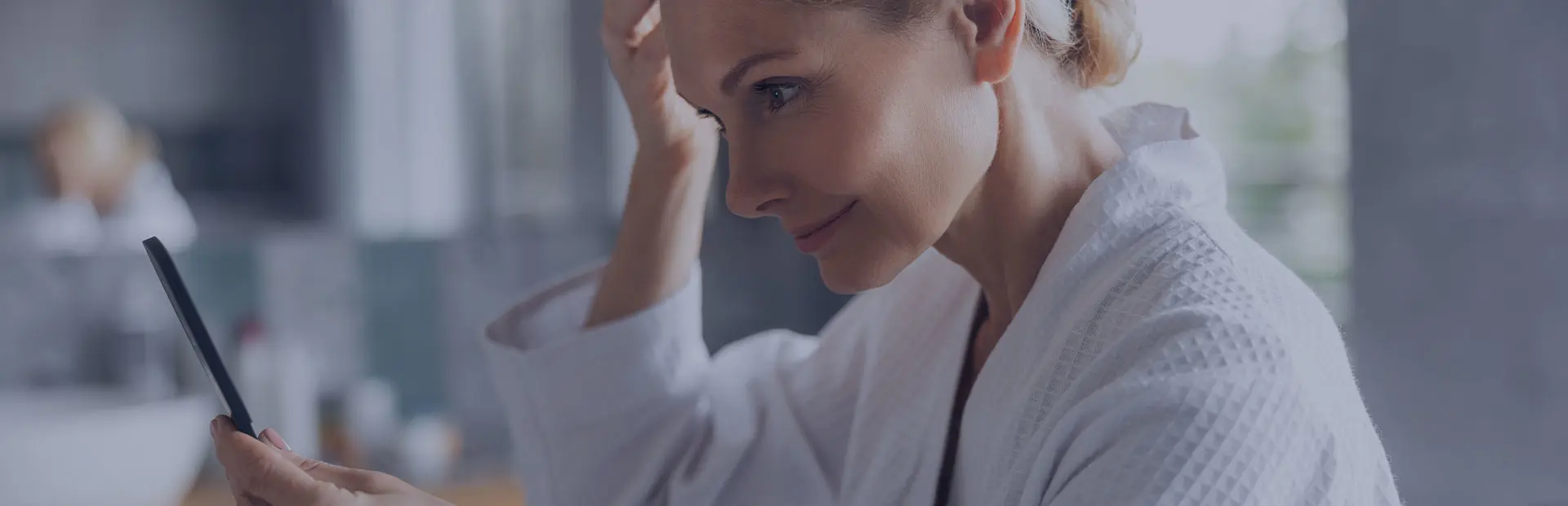 Une femme d'une cinquantaine d'années en robe de chambre blanche se regarde dans un miroir avec assurance, car elle sait comment détourner l'attention de son dentier.