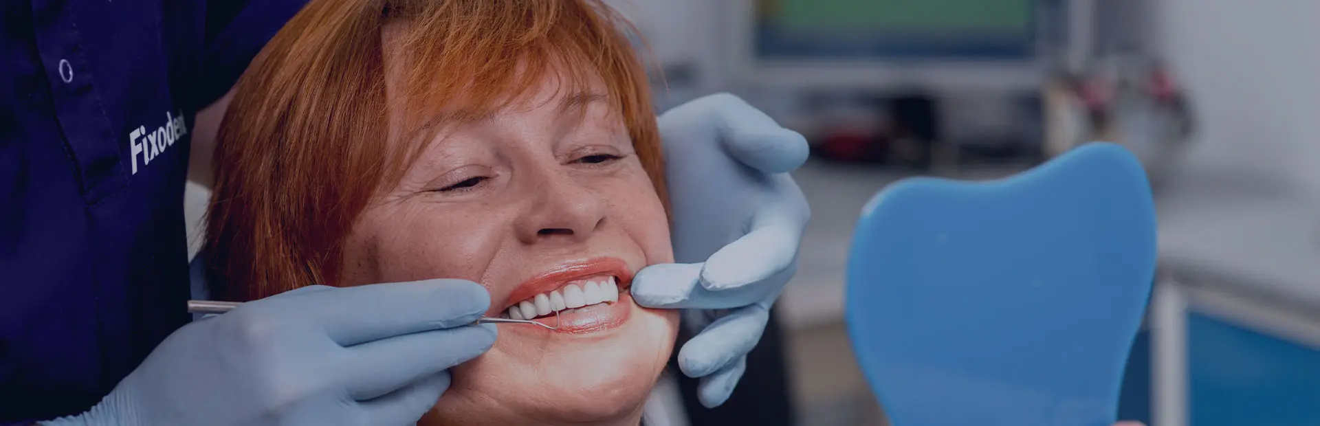 Une femme d'une soixantaine d'années assise sur le fauteuil du dentiste souris, car elle connaît les questions à poser son dentiste.