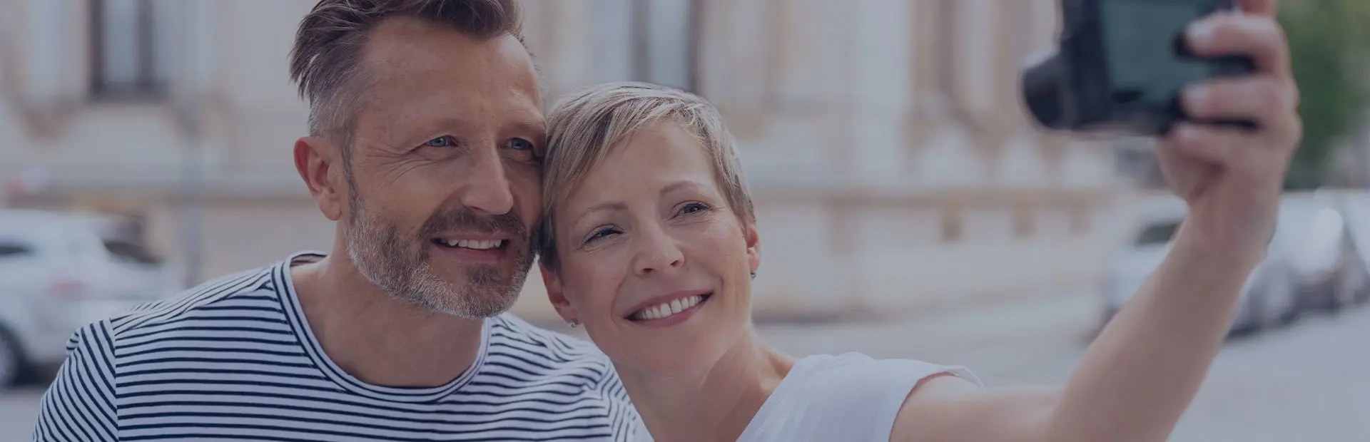 Un couple dans un parc prend une photo d'eux-mêmes, ils ont tous les deux un sourire blanc et brillant, même si l'un d'entre eux porte une prothèse dentaire partielle.