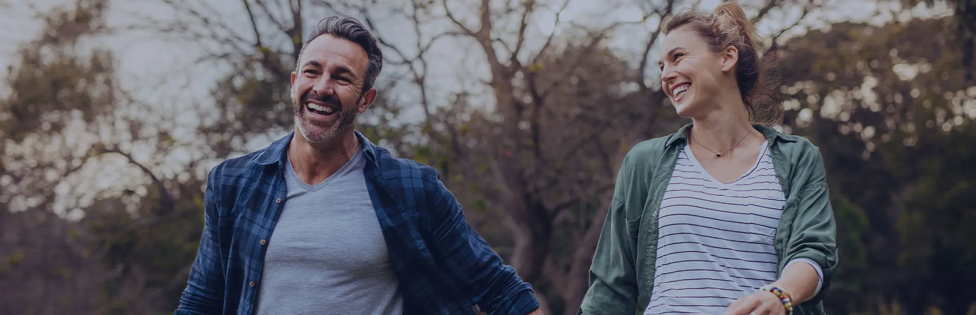 Un couple se tient la main en se promenant dans un parc. Tous les deux sourient car ils savent comment avoir des prothèses dentaires à l'aspect naturel.