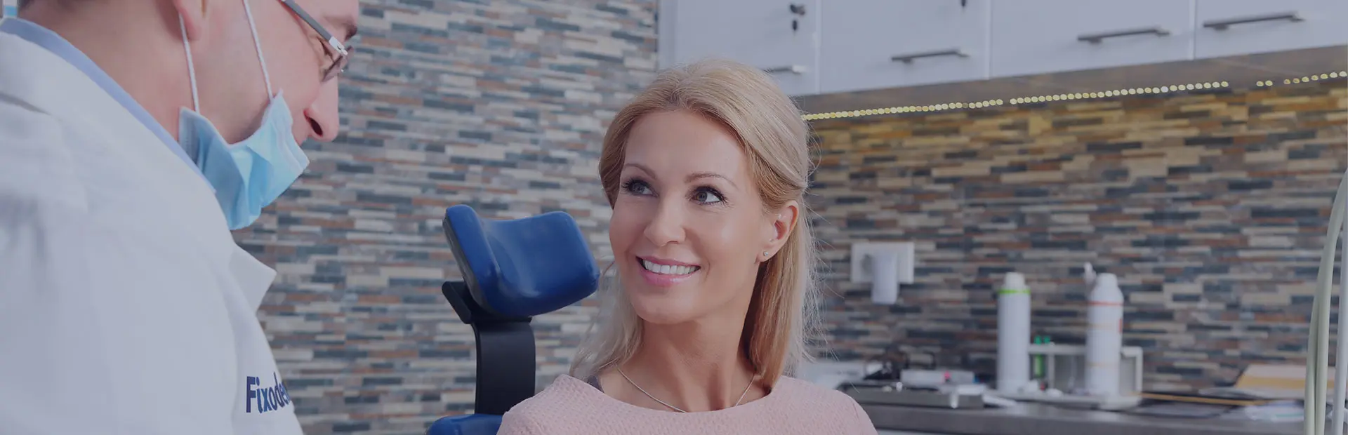 Une femme est assise dans le fauteuil du dentiste et celui-ci lui explique ce que sont les prothèses stellites.