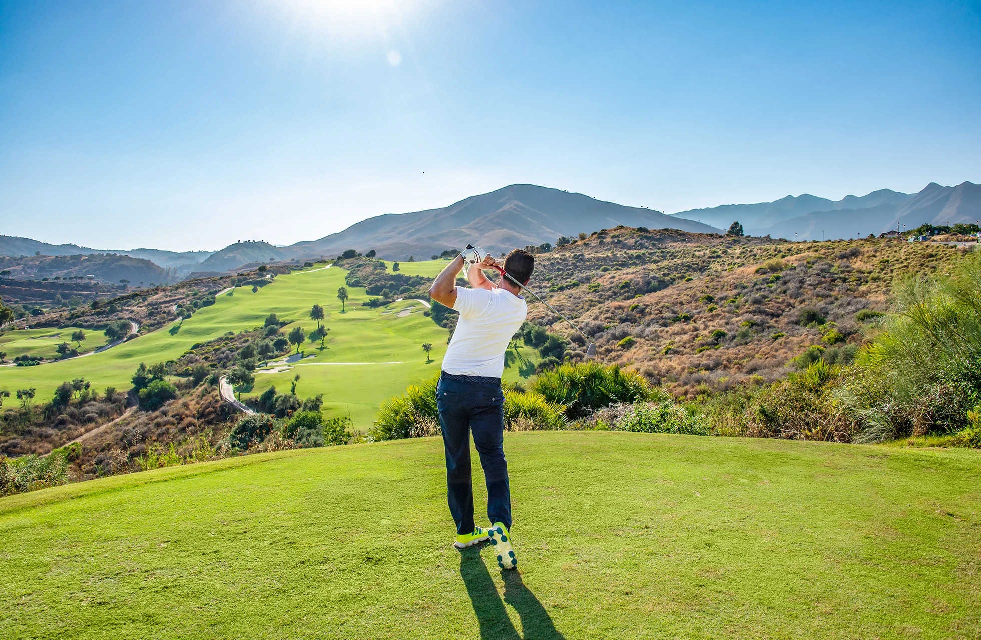 golfspiller slår ut fra tee på la cala europa course med utsikt over grønn dal og fjellandskap