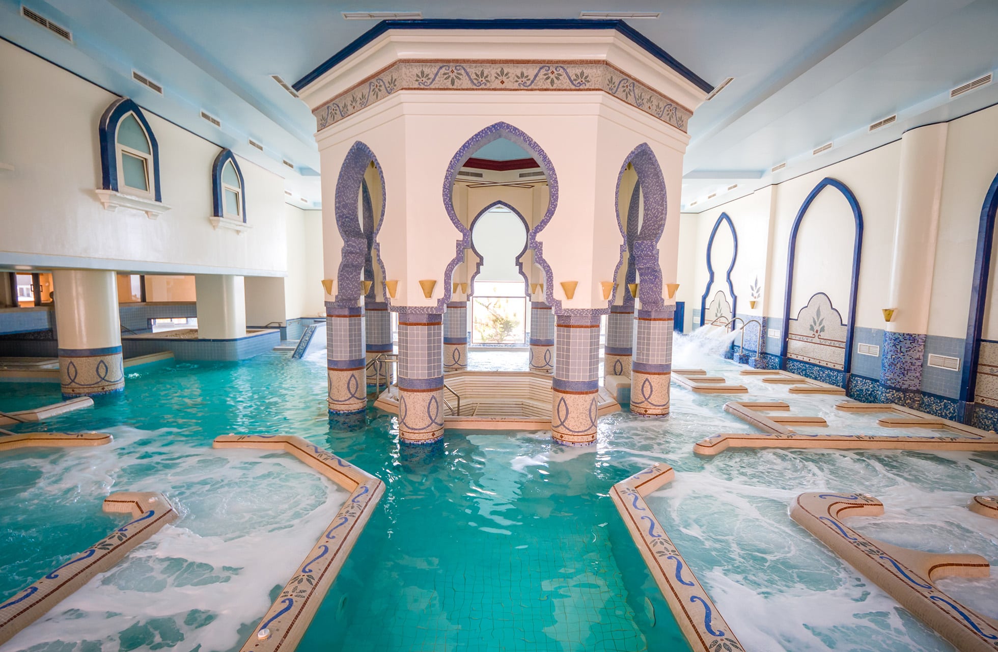 innendørsbasseng med turkist vann, boblebad og dekorative buer i lys arkitektur med orientalske detaljer