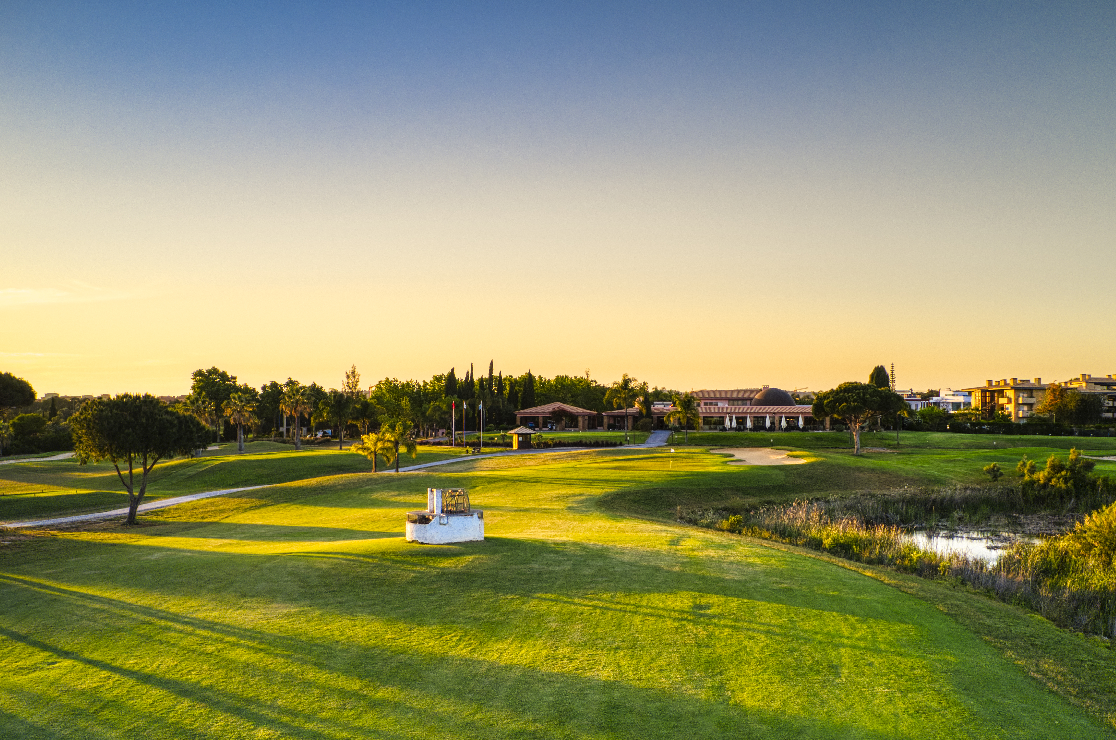 näkymä golfkentälle, taustalla klubitalo ja pitkät puiden varjot ilta-auringossa