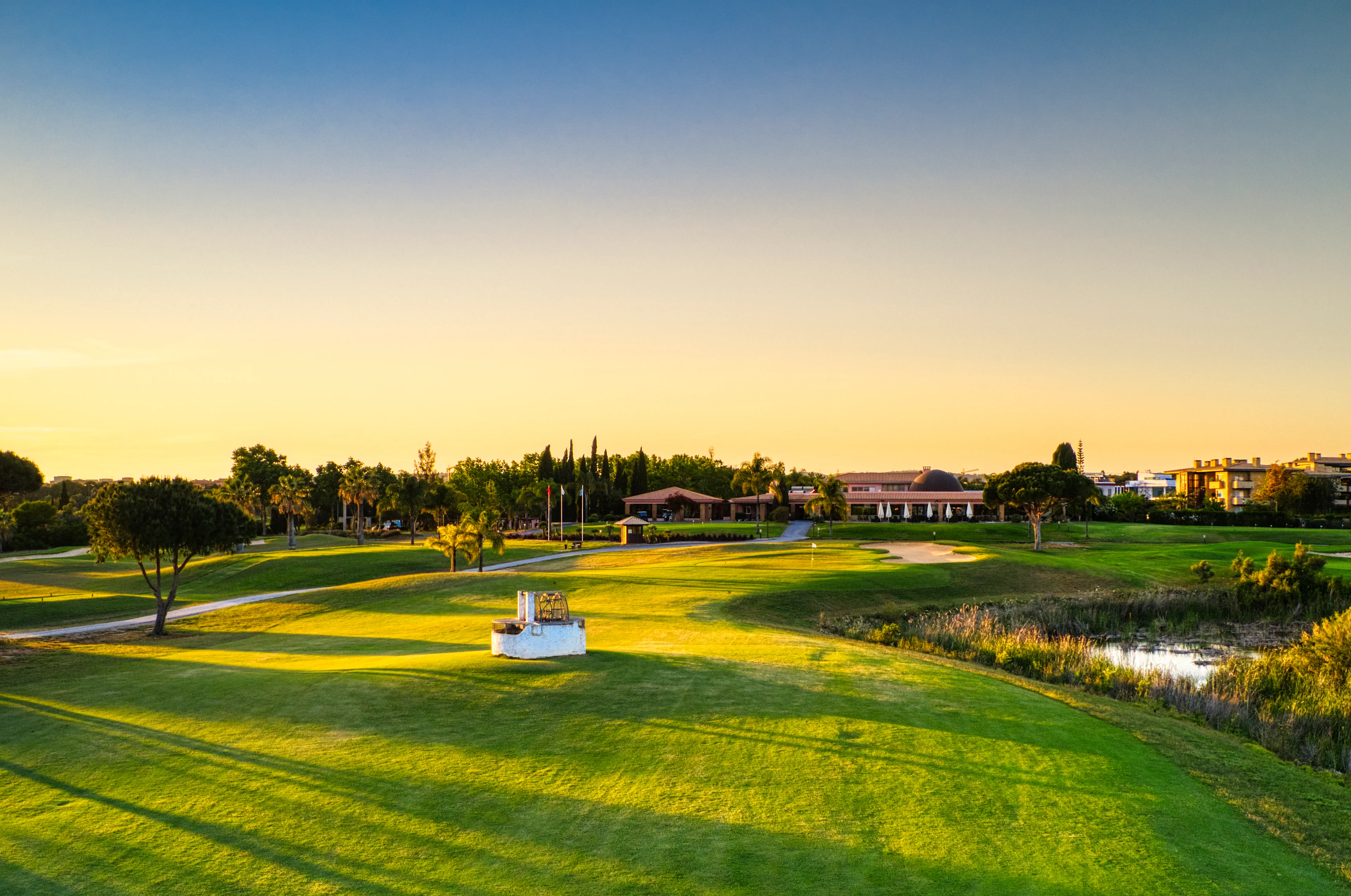 näkymä golfkentälle, taustalla klubitalo ja pitkät puiden varjot ilta-auringossa
