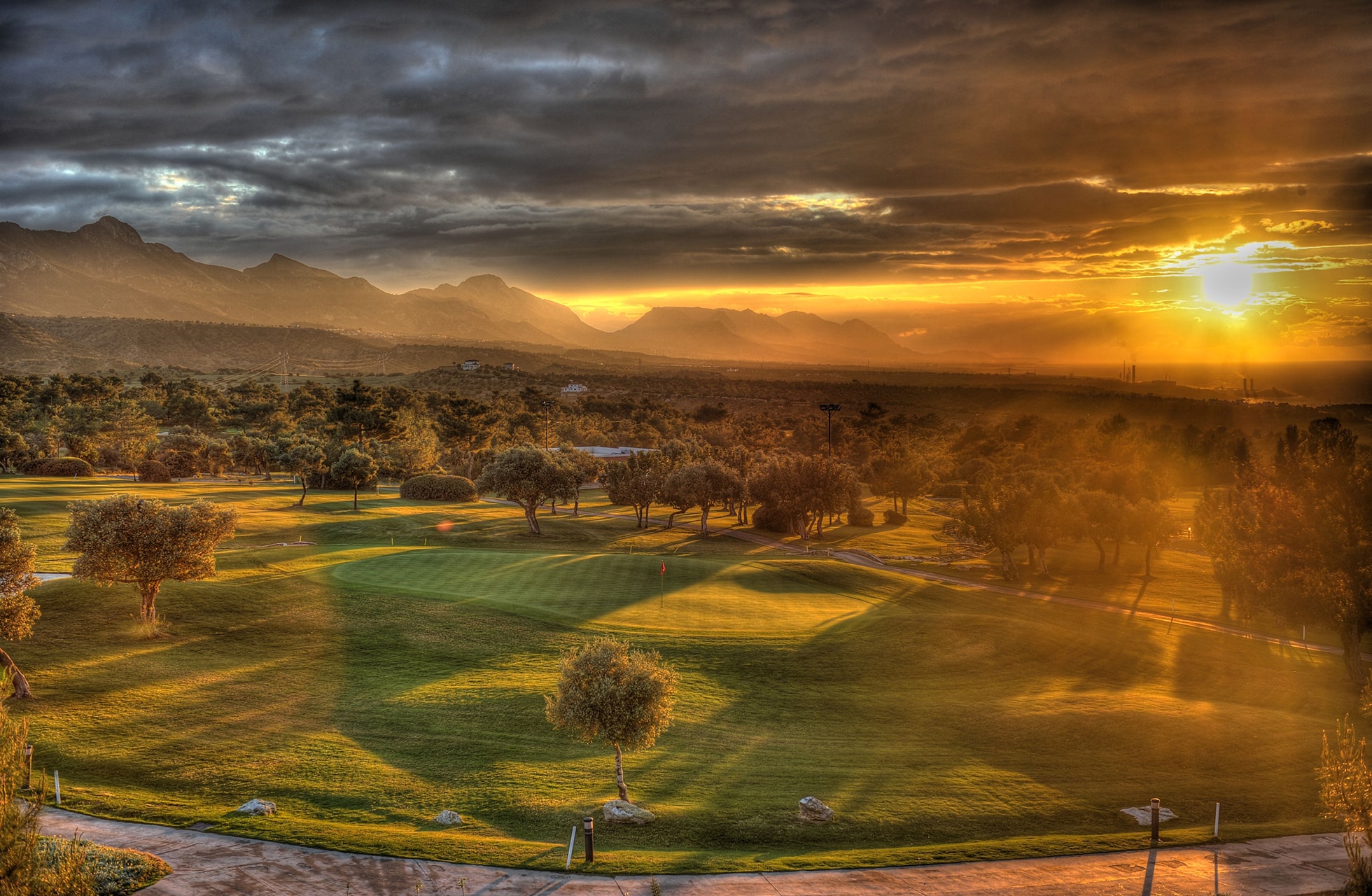 utsikt over korineum golf club i solnedgang med grønne fairways, trær og fjell i bakgrunnen