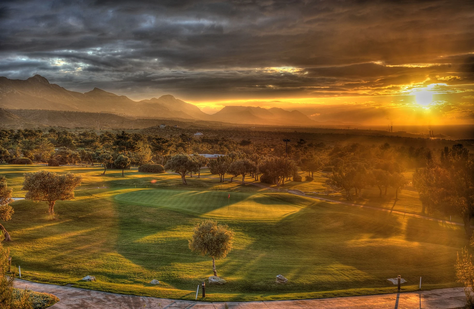 utsikt over korineum golf club i solnedgang med grønne fairways, trær og fjell i bakgrunnen