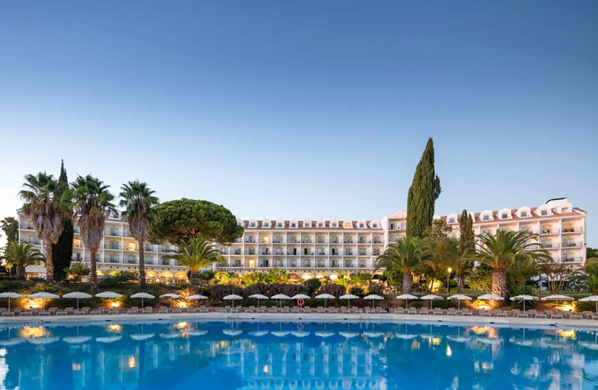 kveldsbilde av penina hotel & golf resort i algarve med opplyst basseng, palmer og hotellbygning i bakgrunnen