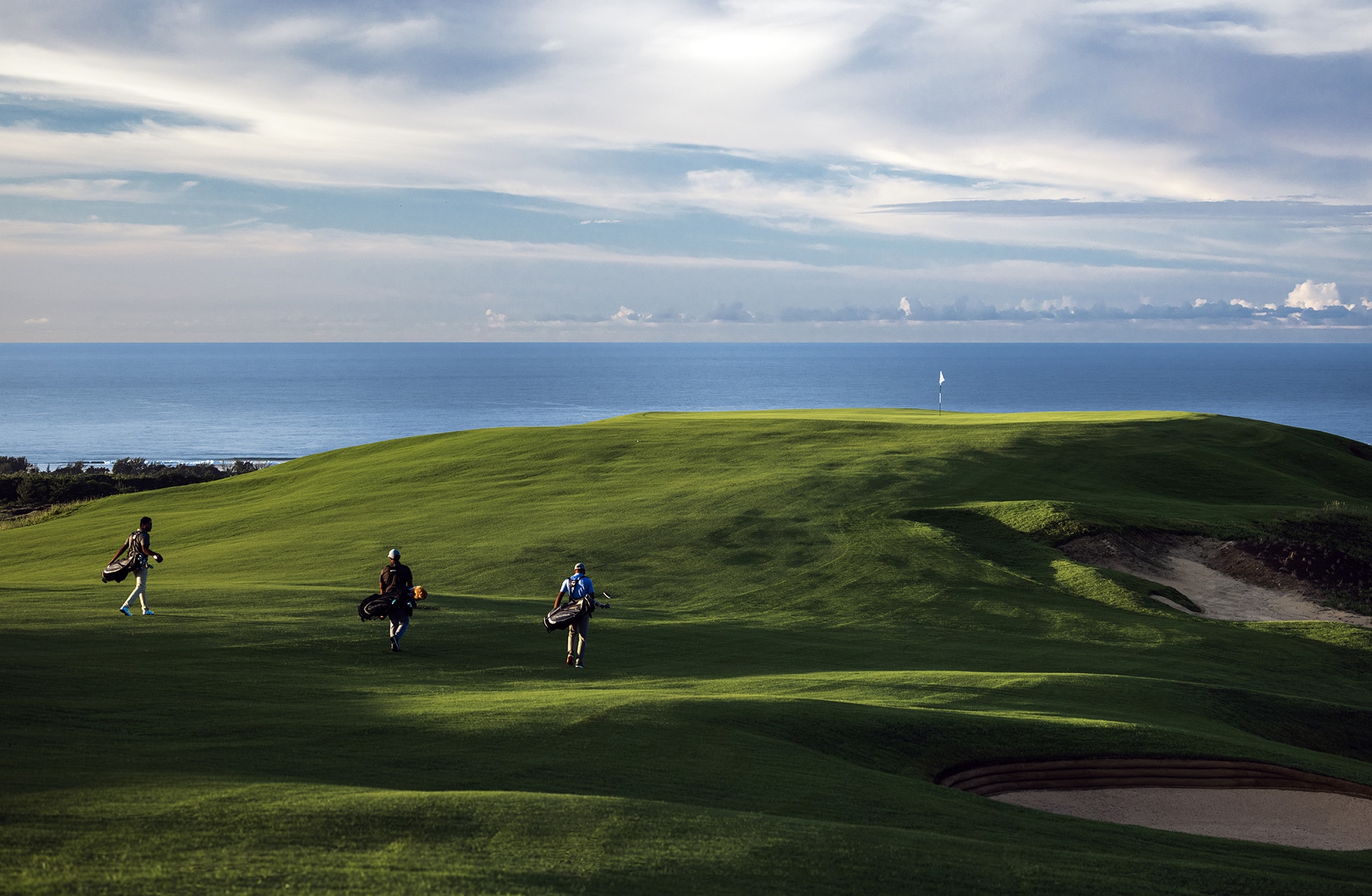 golfspillere går over bølgende green på heritage golf club la réserve golf links med bunker og åbent hav i baggrunden