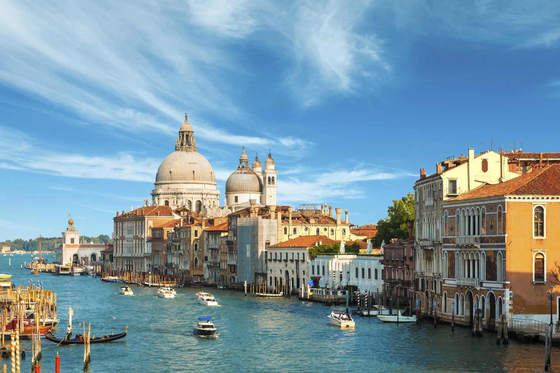 näkymä venetsian canal grandelle, santa maria della salute -basilika, historiallisia rakennuksia ja veneitä veden äärellä kirkkaan sinisen taivaan alla