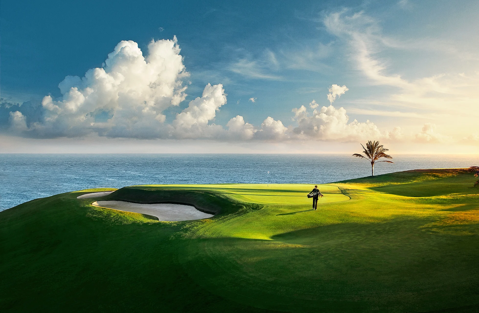 grønn golfbane ved havet med bunker i forgrunnen, en spiller på fairway, palmer og dramatisk himmel i mykt kveldslys.