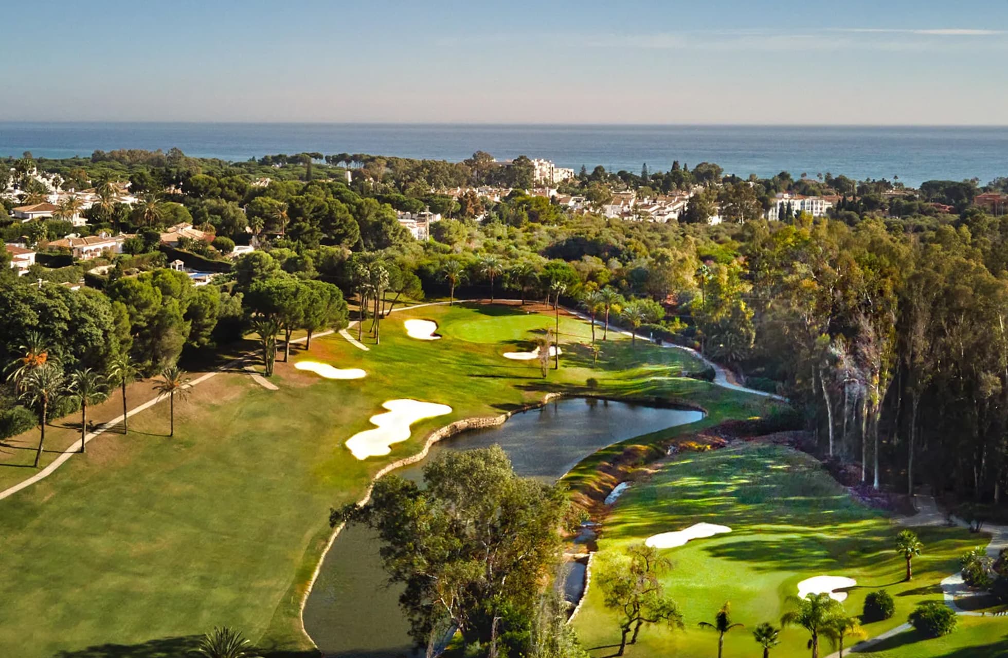 flyfoto av el paraiso golf med green, fairway, bunkere og vannparti i parklandskap, med bebyggelse og havet i bakgrunnen