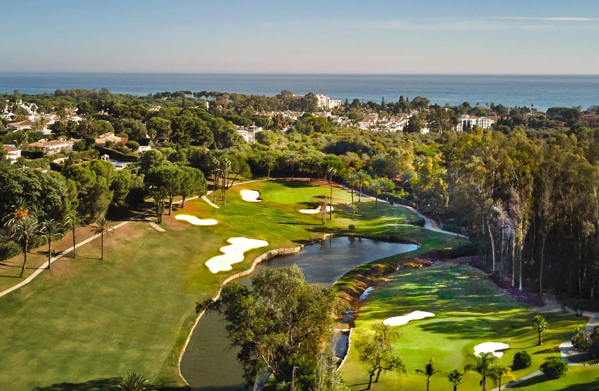 flyfoto av el paraiso golf med green, fairway, bunkere og vannparti i parklandskap, med bebyggelse og havet i bakgrunnen