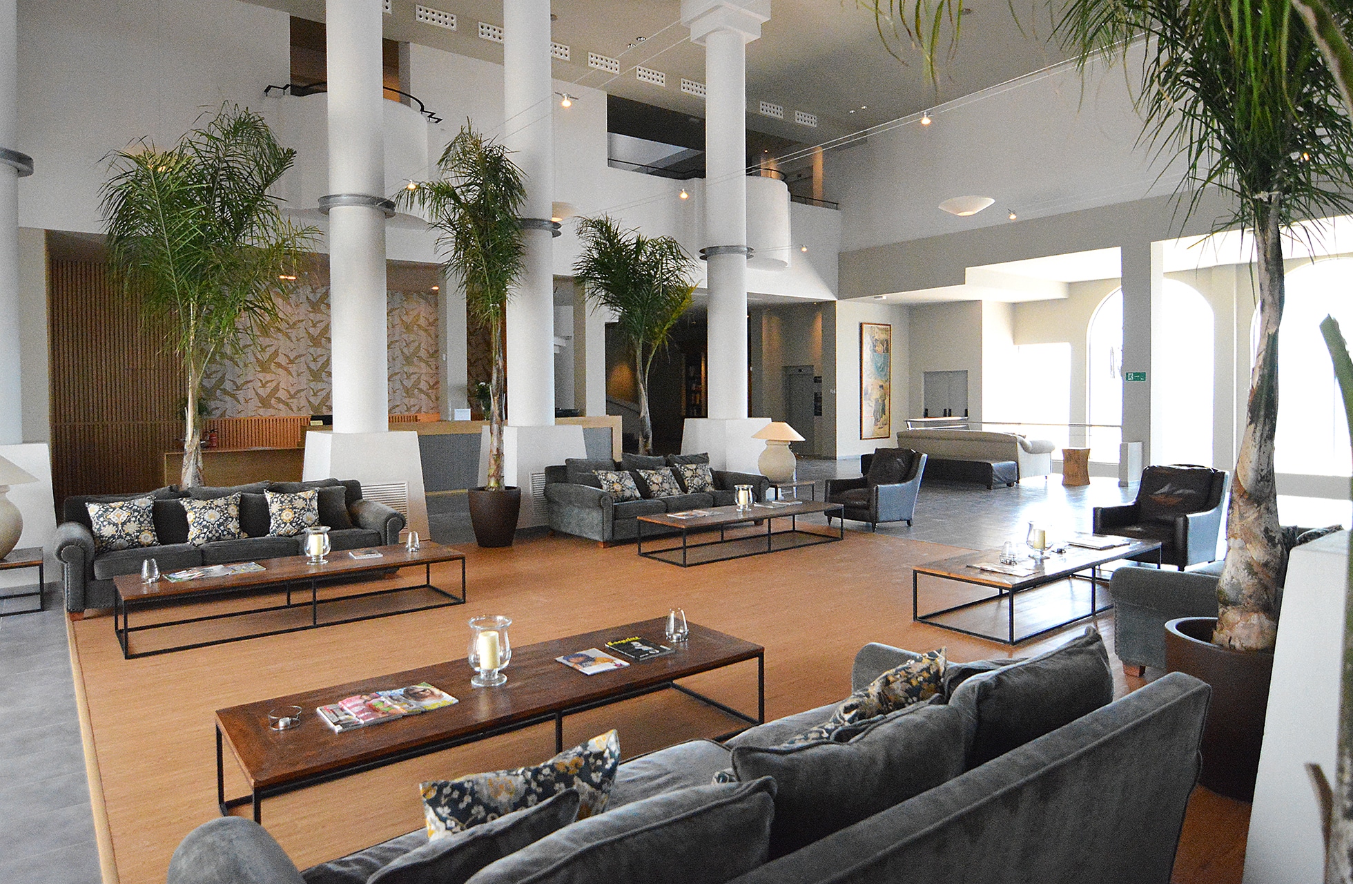 romslig hotellobby med høyt under taket, sittegrupper, søyler og grønne planter i lys og åpen atmosfære