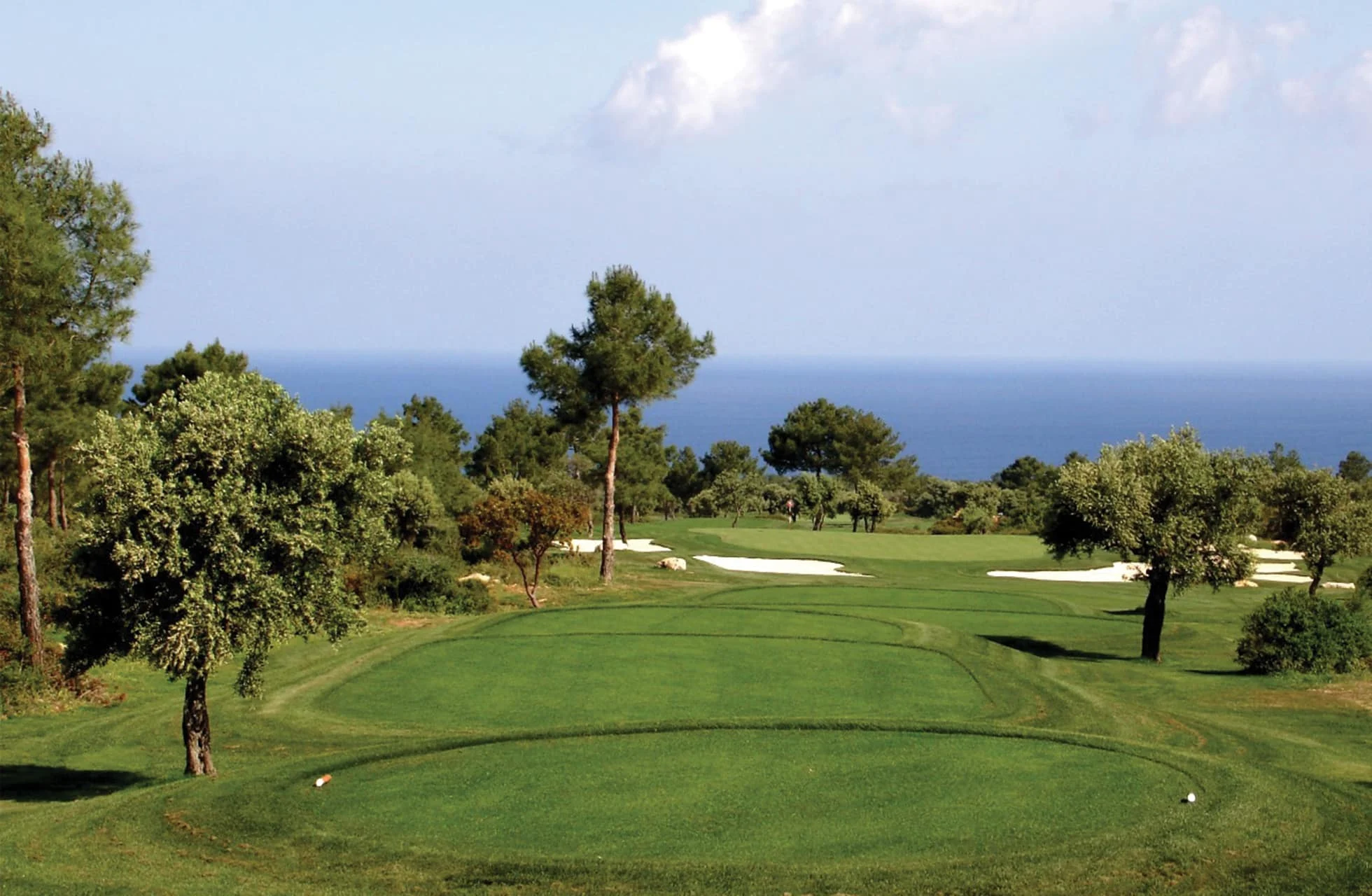 tee-sted på korineum golf country club med velplejet fairway, bunkers og middelhavet i baggrunden