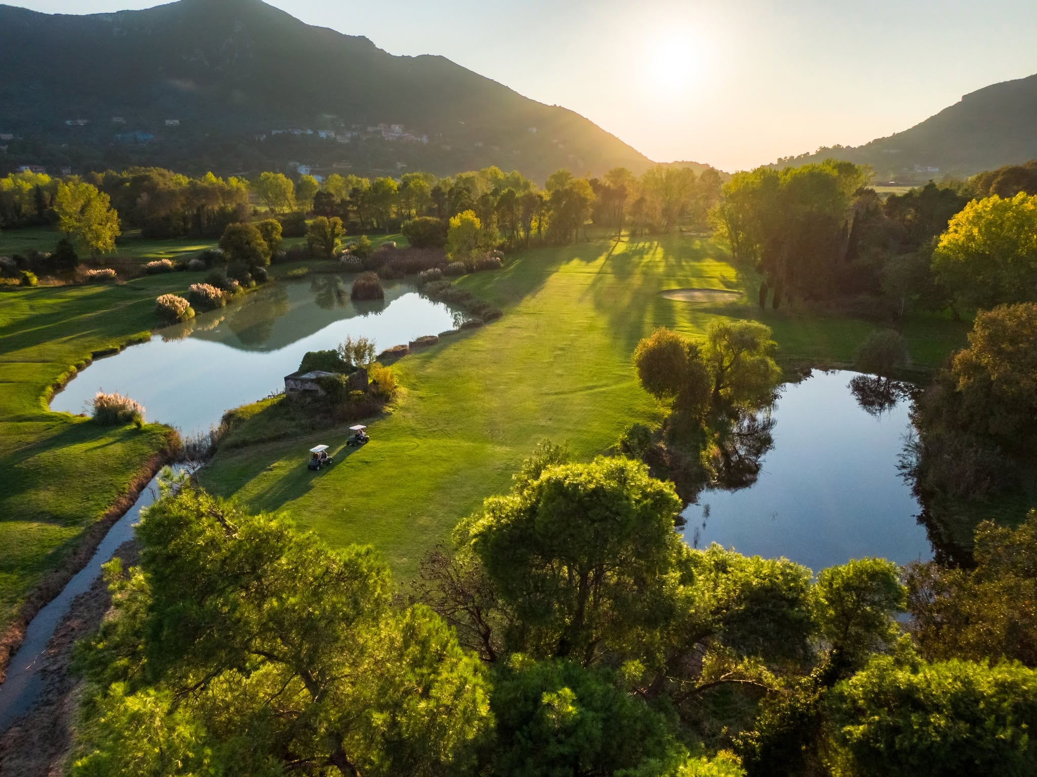 golfbana vid solnedgång med vattenhinder och långa skuggor över greenområden