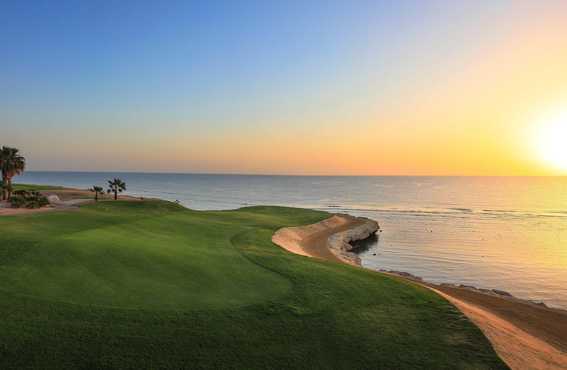 kystnær green på soma bay golf i solnedgang med sandbunkere og havet rett ved banen
