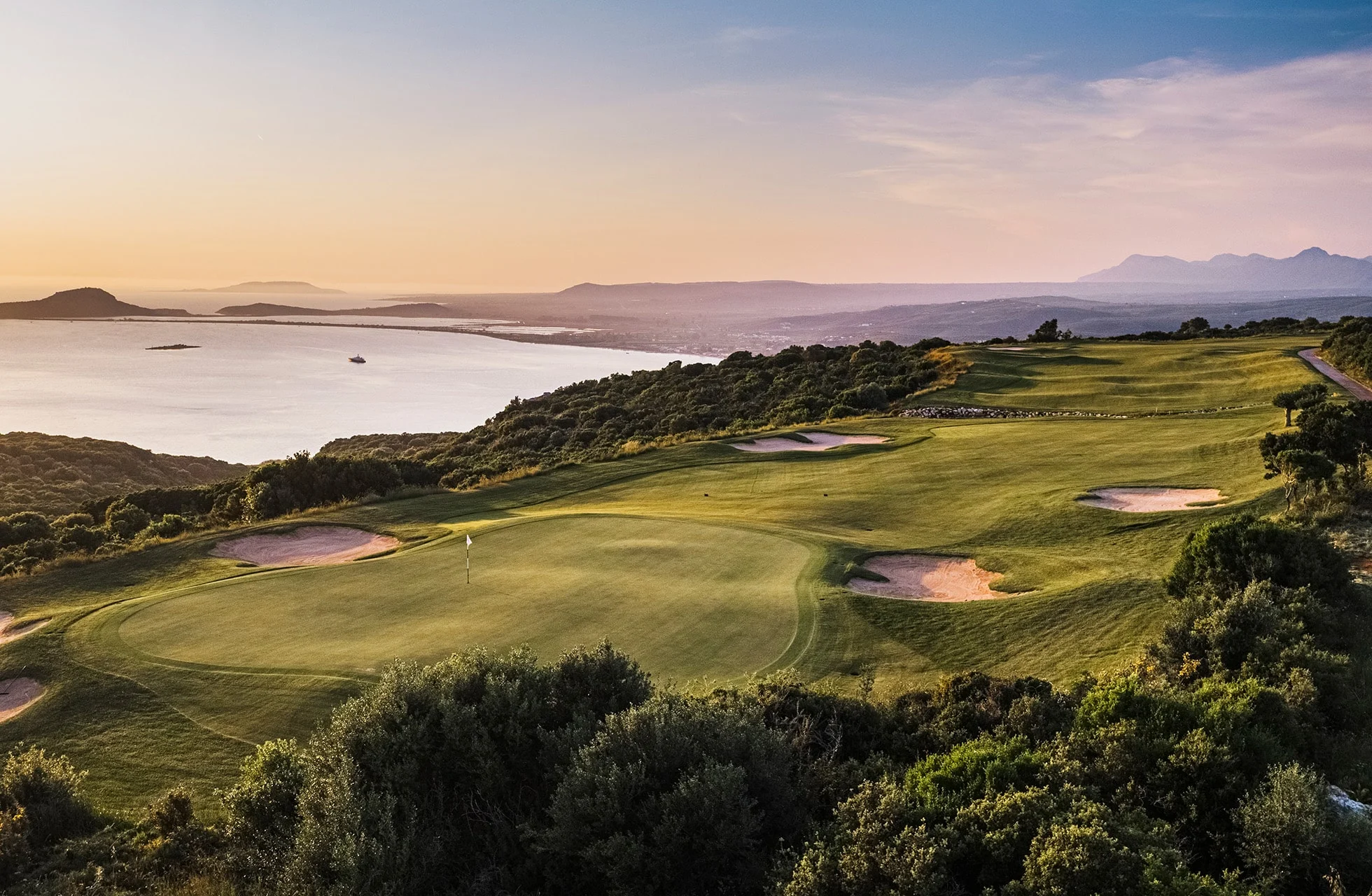 utsikt over green med bunkere på the olympic course, costa navarino, med havet og kystlandskap i bakgrunnen i varmt kveldslys