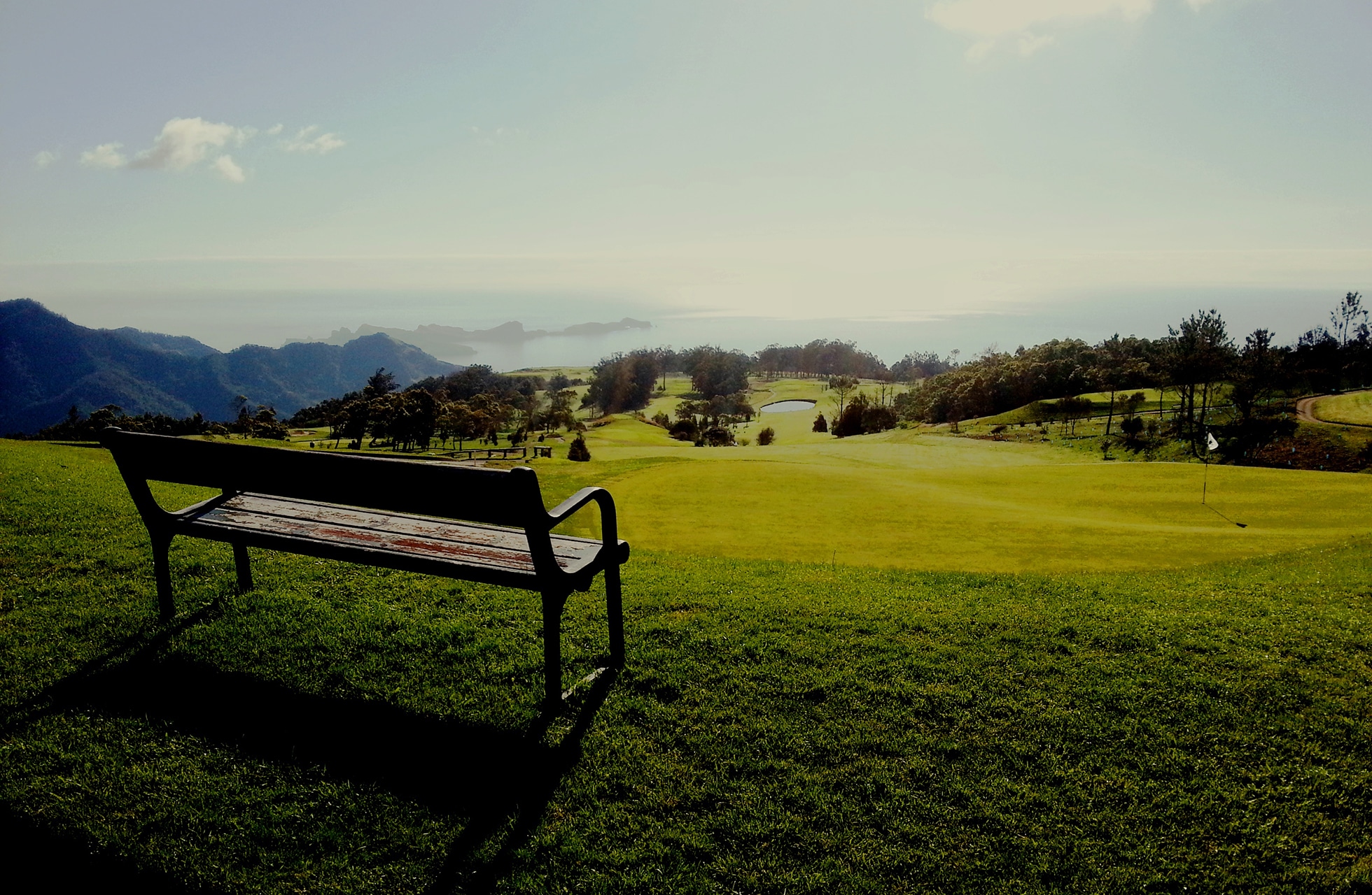 benk ​​i forgrunnen med utsikt over golfbanen og havet