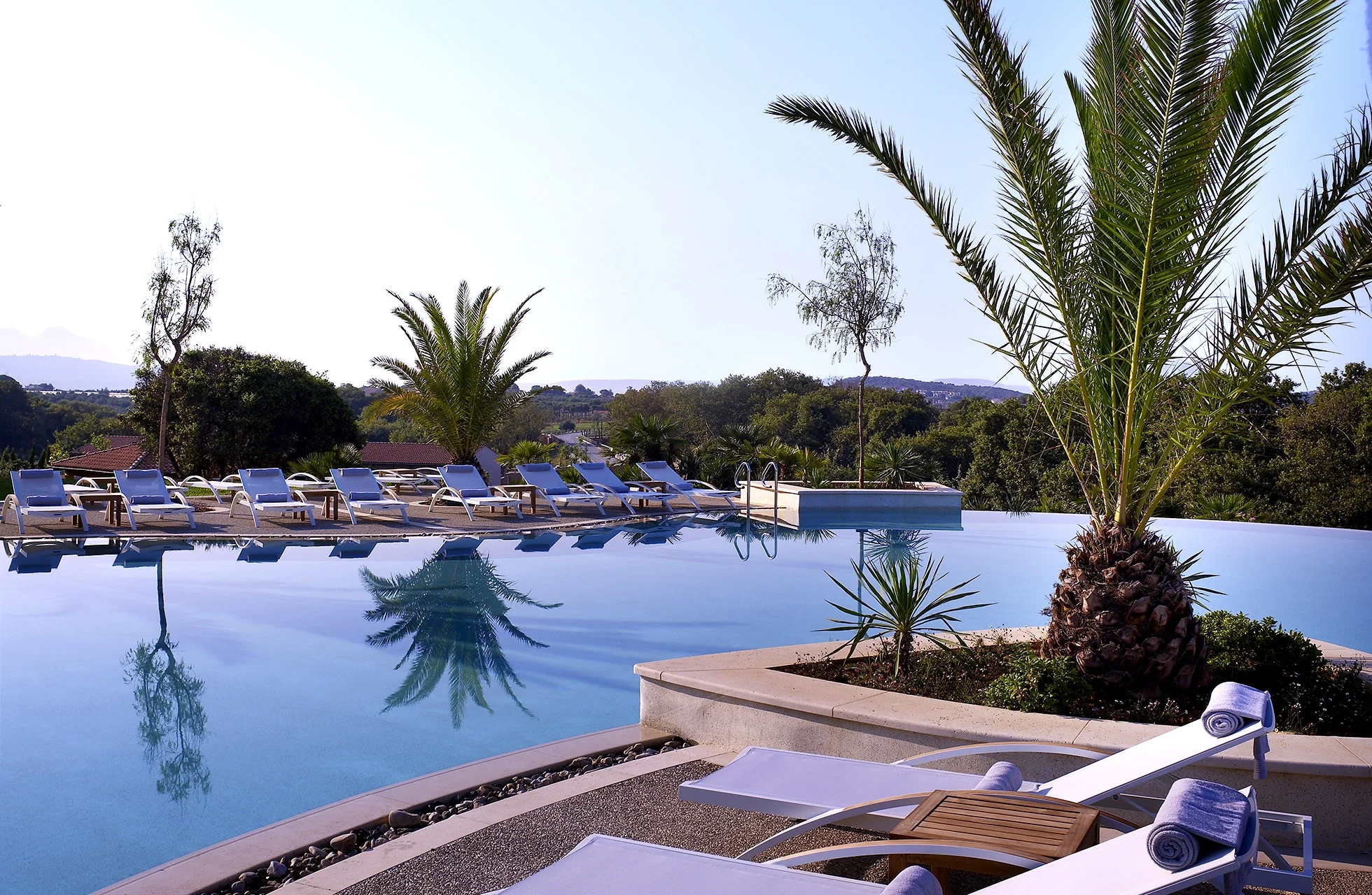 utendørsbasseng på the westin costa navarino med solsenger, palmer og utsikt over grønt landskap