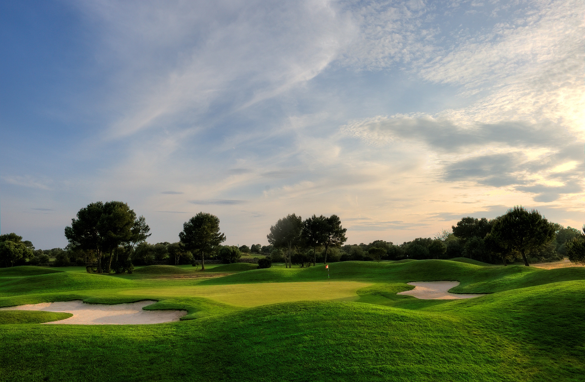 golfgreen på son antem golf omgitt av flere bunkere og bølgende fairwayer i åpent parklandskap i varmt kveldslys
