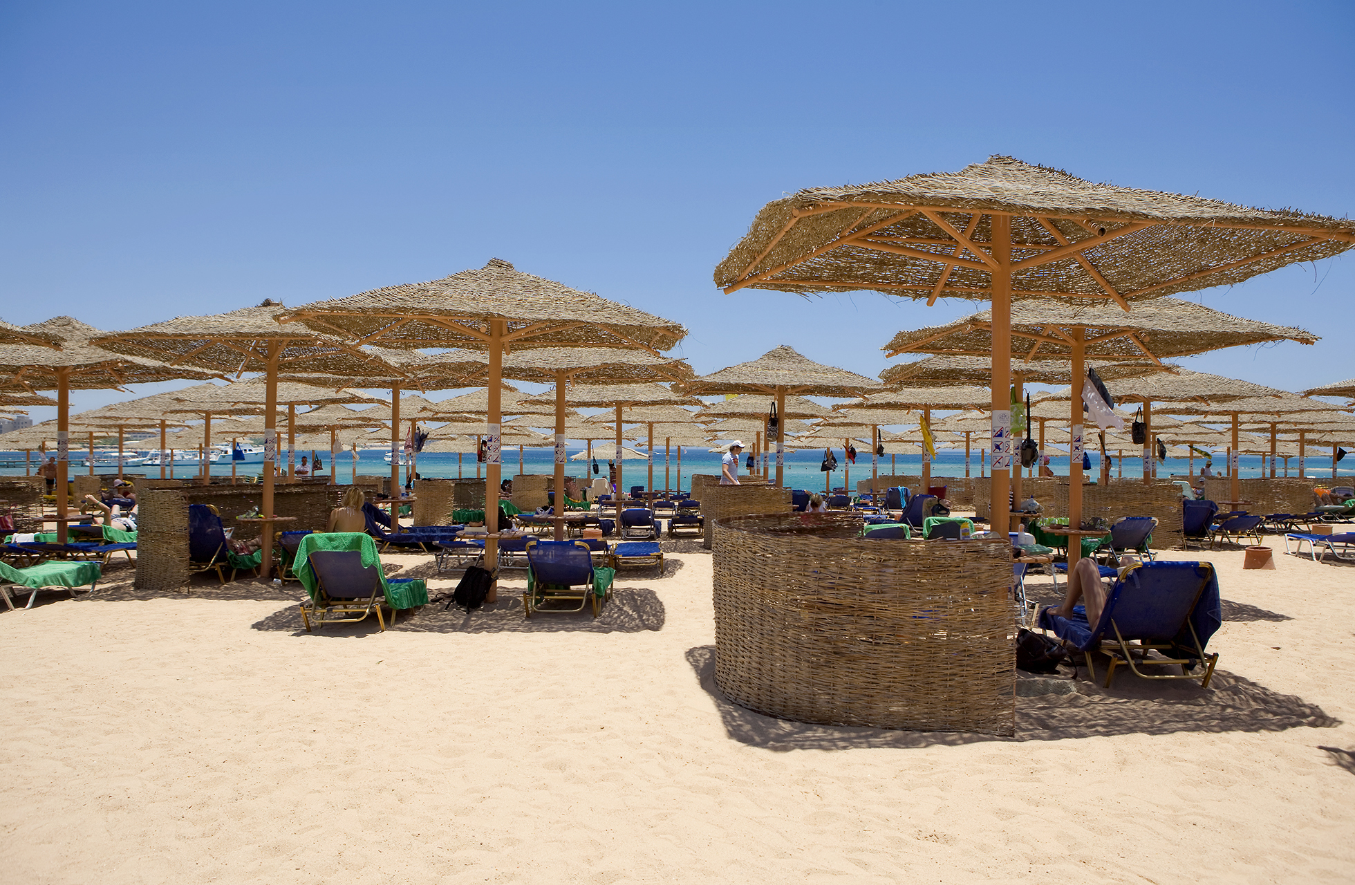 sandstrand med mange solsenger under stråparasoller, med turkist hav og klar blå himmel i bakgrunnen