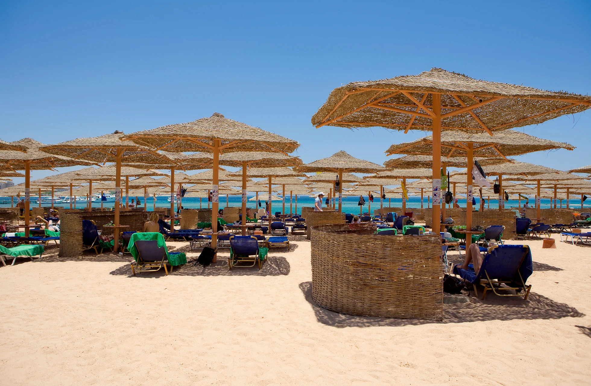 sandstrand med mange solsenger under stråparasoller, med turkist hav og klar blå himmel i bakgrunnen