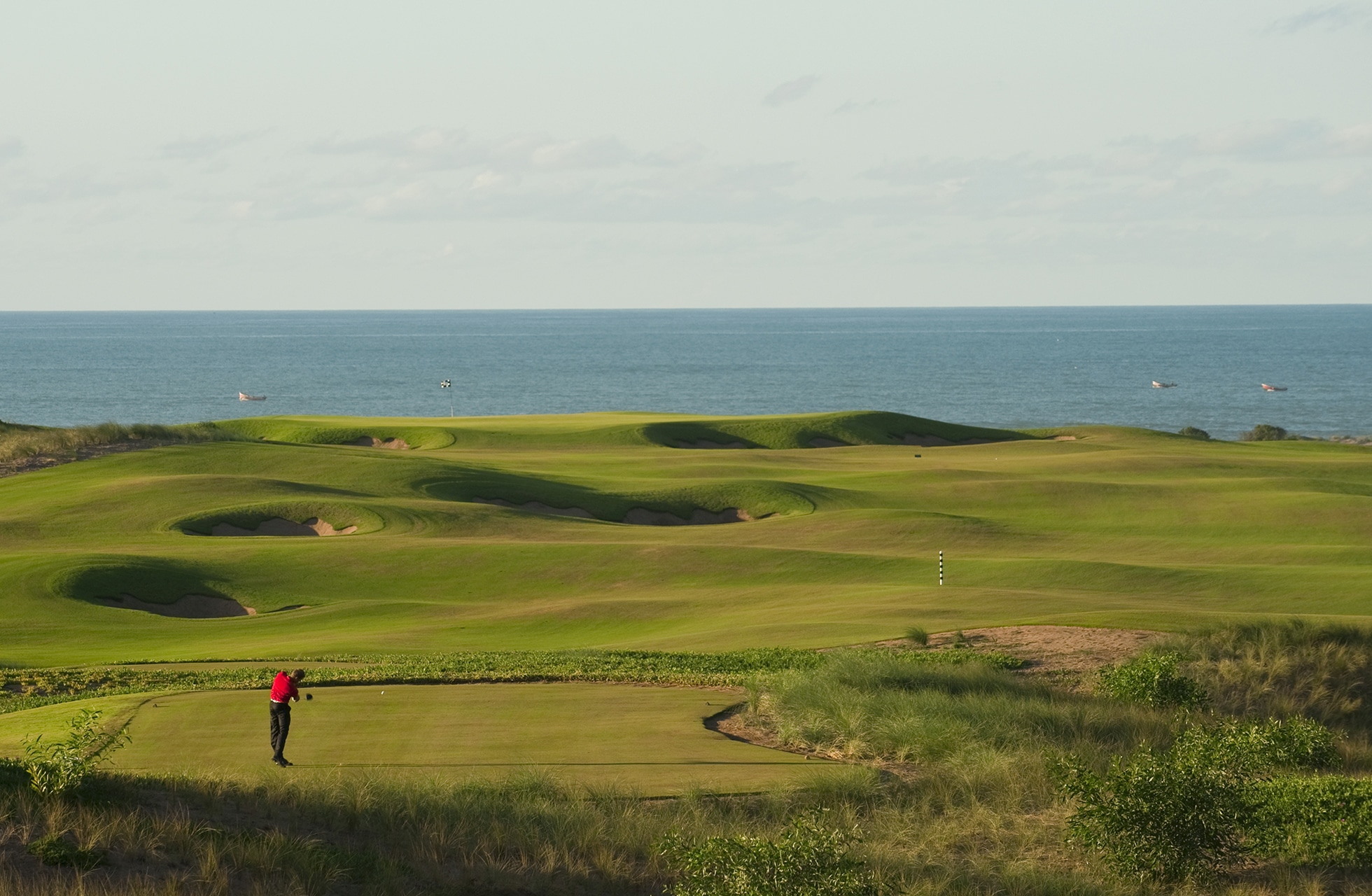 kupert golfbane i kystlandskap med bølgende fairwayer og green, én golfspiller i forgrunnen og havet i bakgrunnen