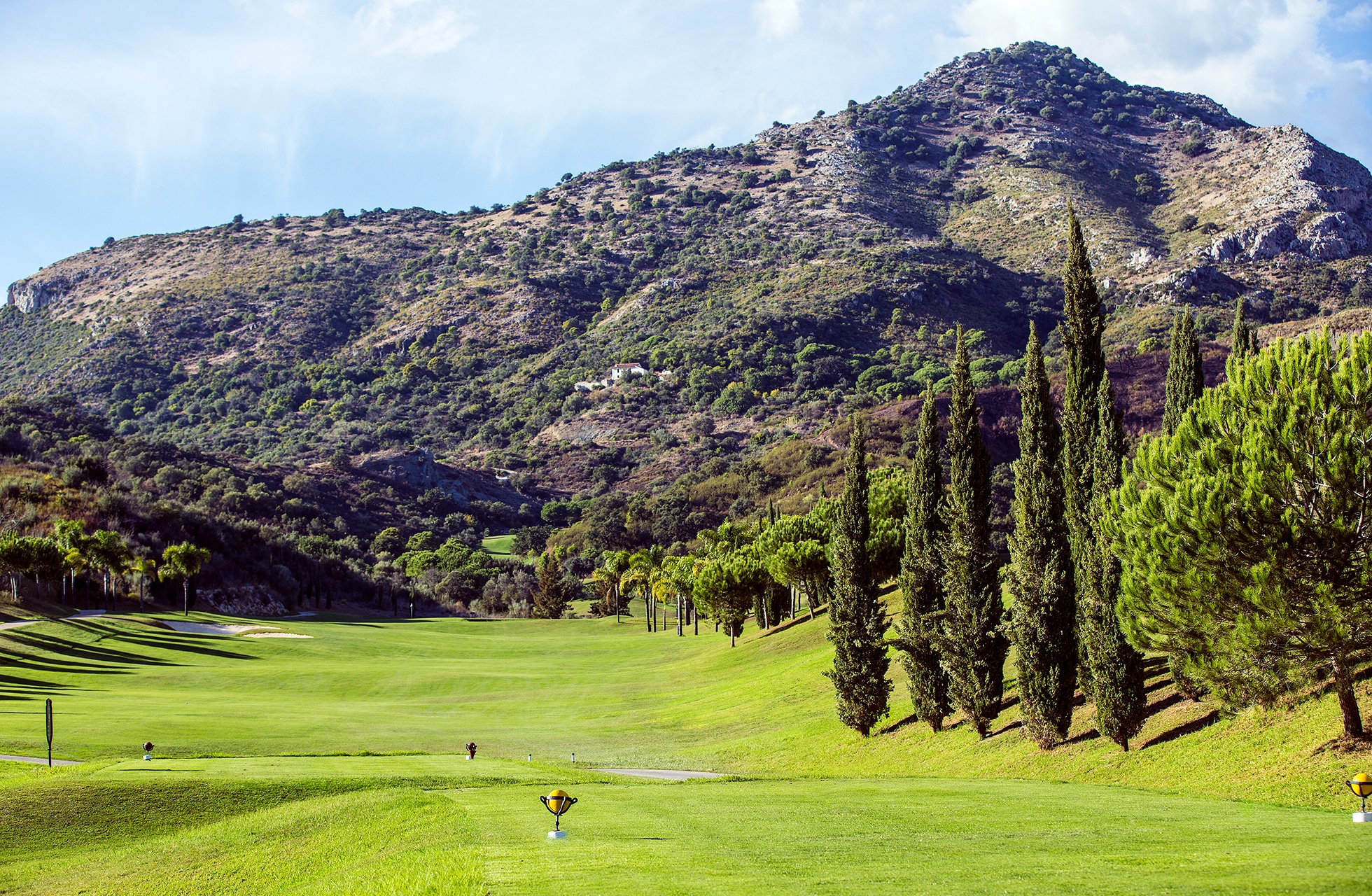 bred fairway på villa padierna golf i åpen dal, kantet av sypresser og trær med fjell i bakgrunnen i mykt dagslys