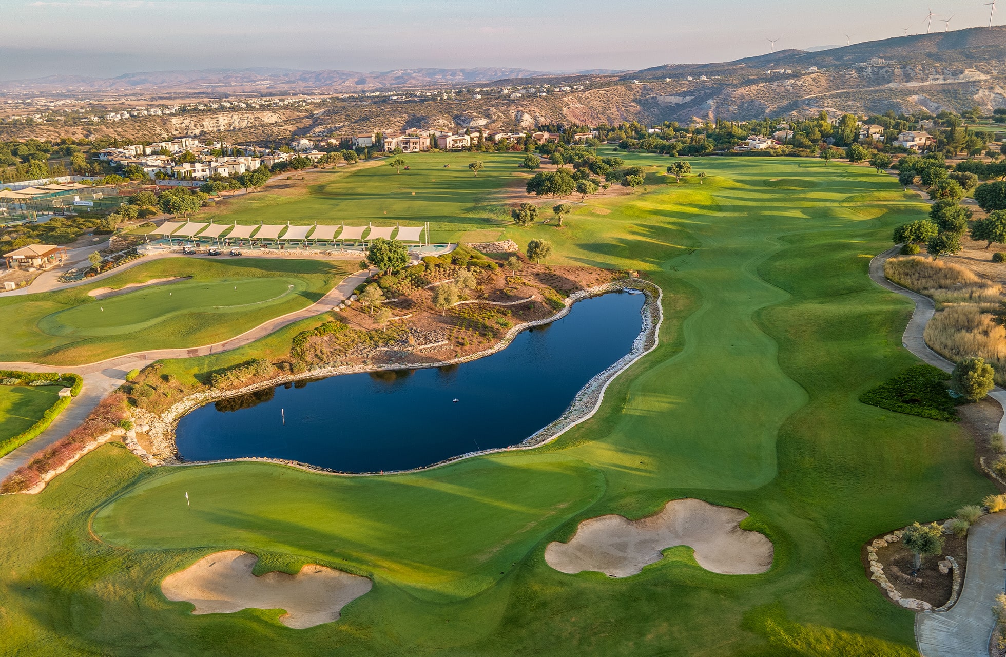 flyfoto av aphrodite hills golf med fairways, bunkere og vannhinder i kupert landskap