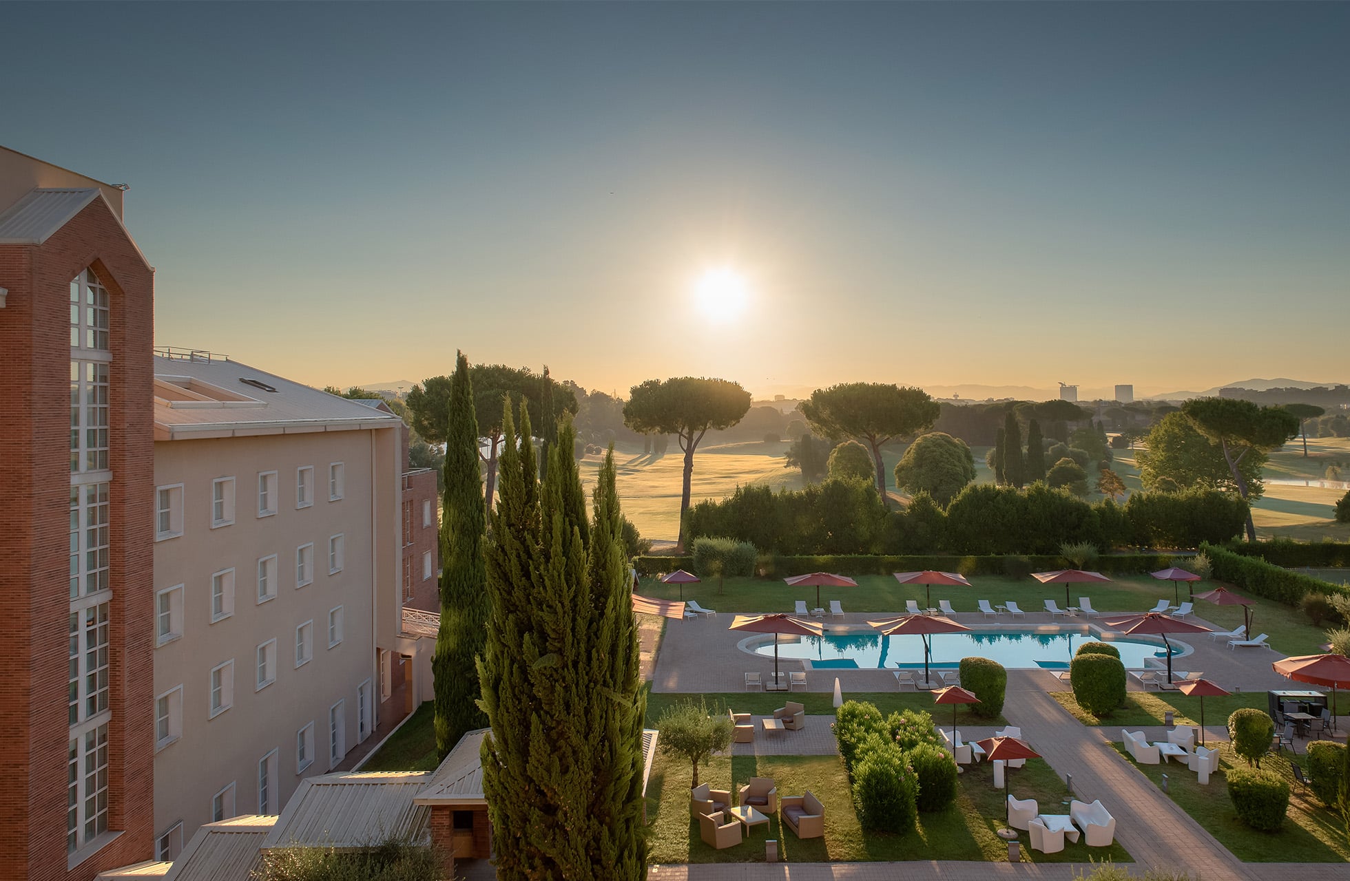 bassengområde ved hotellet i soloppgang med solsenger, parasoller og grønt landskap