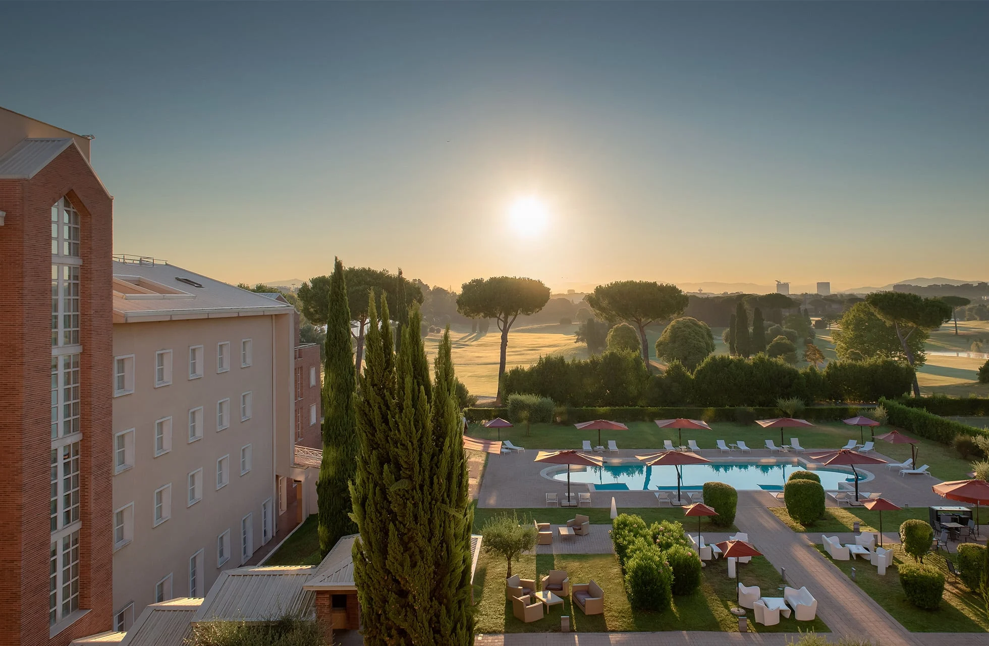 bassengområde ved hotellet i soloppgang med solsenger, parasoller og grønt landskap