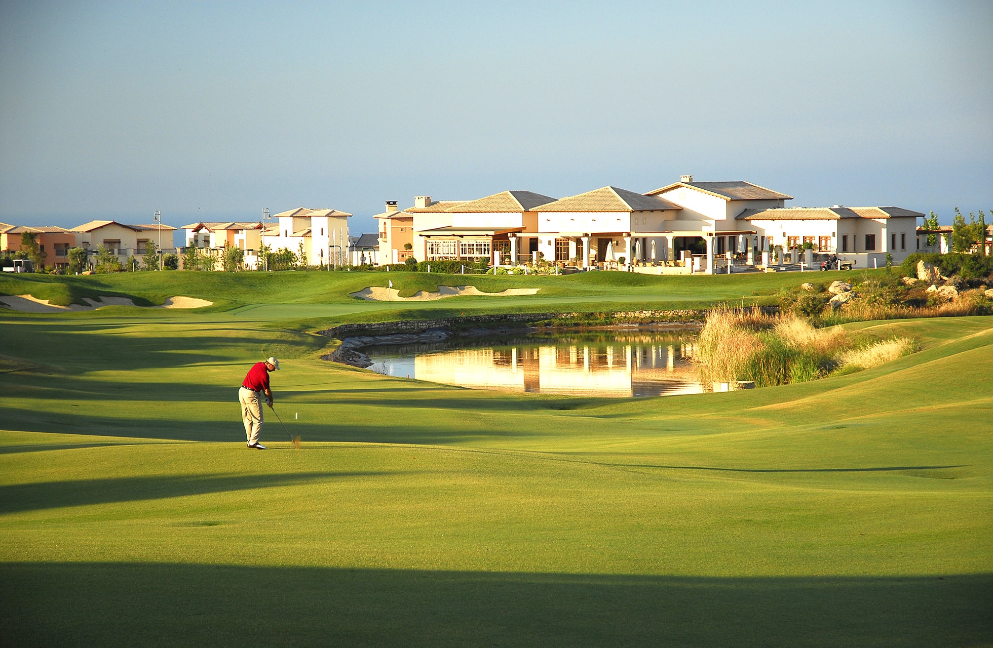 Golfspiller slår ut mot greenen på Aphrodite Hills Golf med klubbhus i bakgrunnen