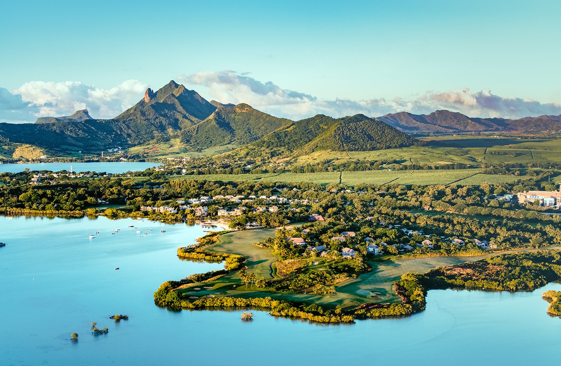 flyfoto av anahita golf club mauritius med golfbane, lagune og bebyggelse i kystlandskap med fjell i bakgrunnen