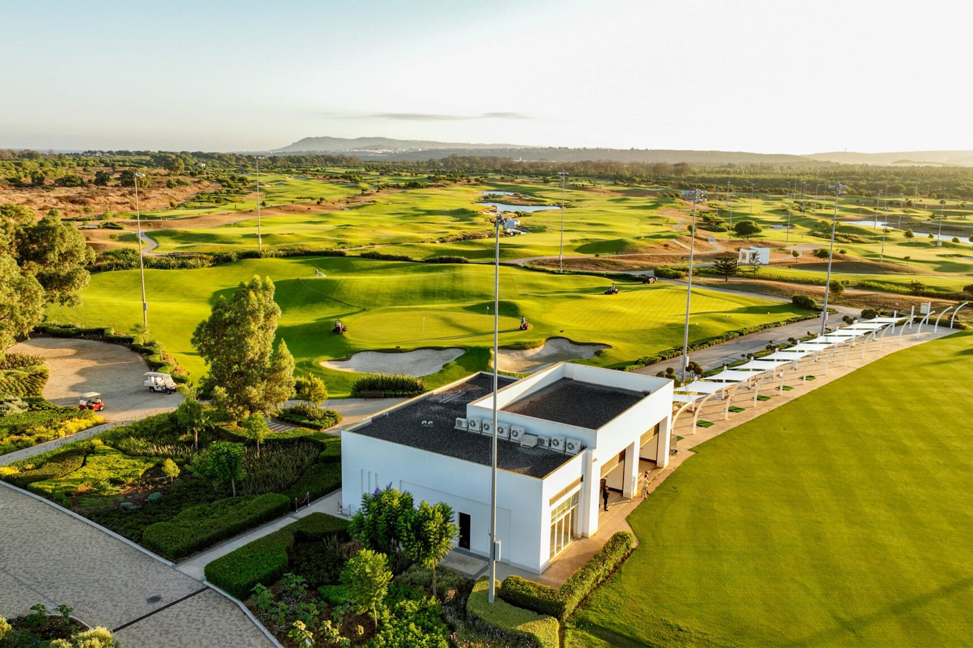 luftfoto af et golfresortområde med moderne klubhus, grønne fairways, greens og stisystem i et åbent landskab.