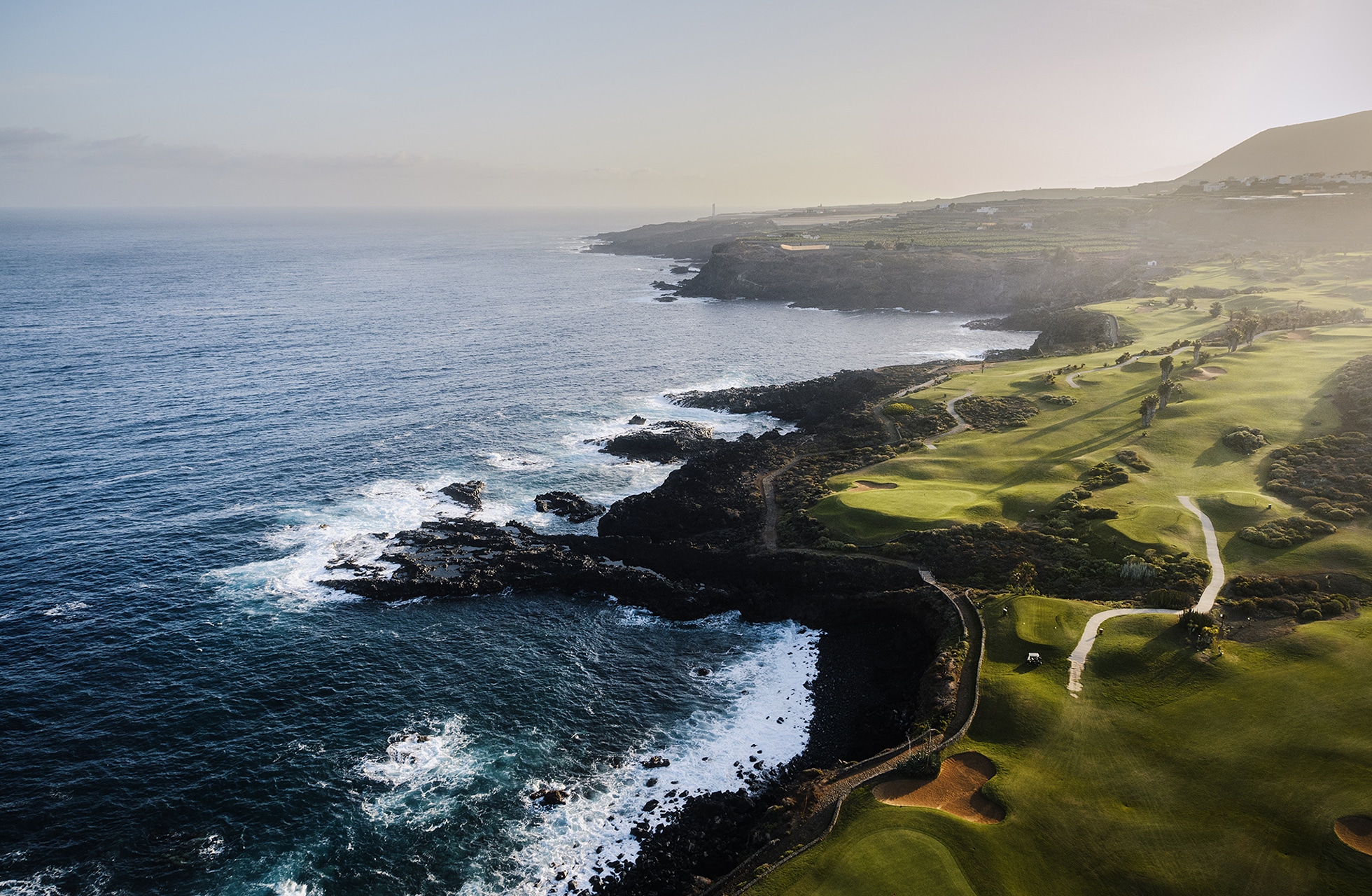 ilmakuva buenavista golfista teneriffalla, jossa vihreät väylät kulkevat dramaattista atlantin rannikkoa pitkin.