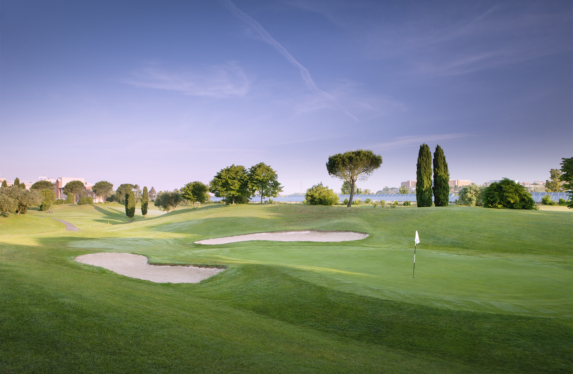 utsikt over green med flere sandbunkere og flagg på parco de’ medici golf club, omgitt av fairwayer og trær