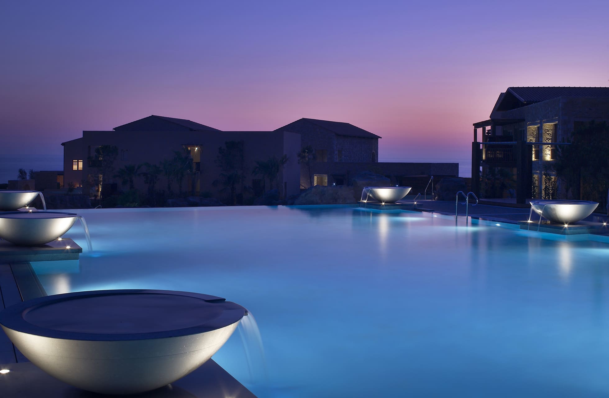 opplyst infinitybasseng på the westin costa navarino i skumring med hotellbygninger i bakgrunnen