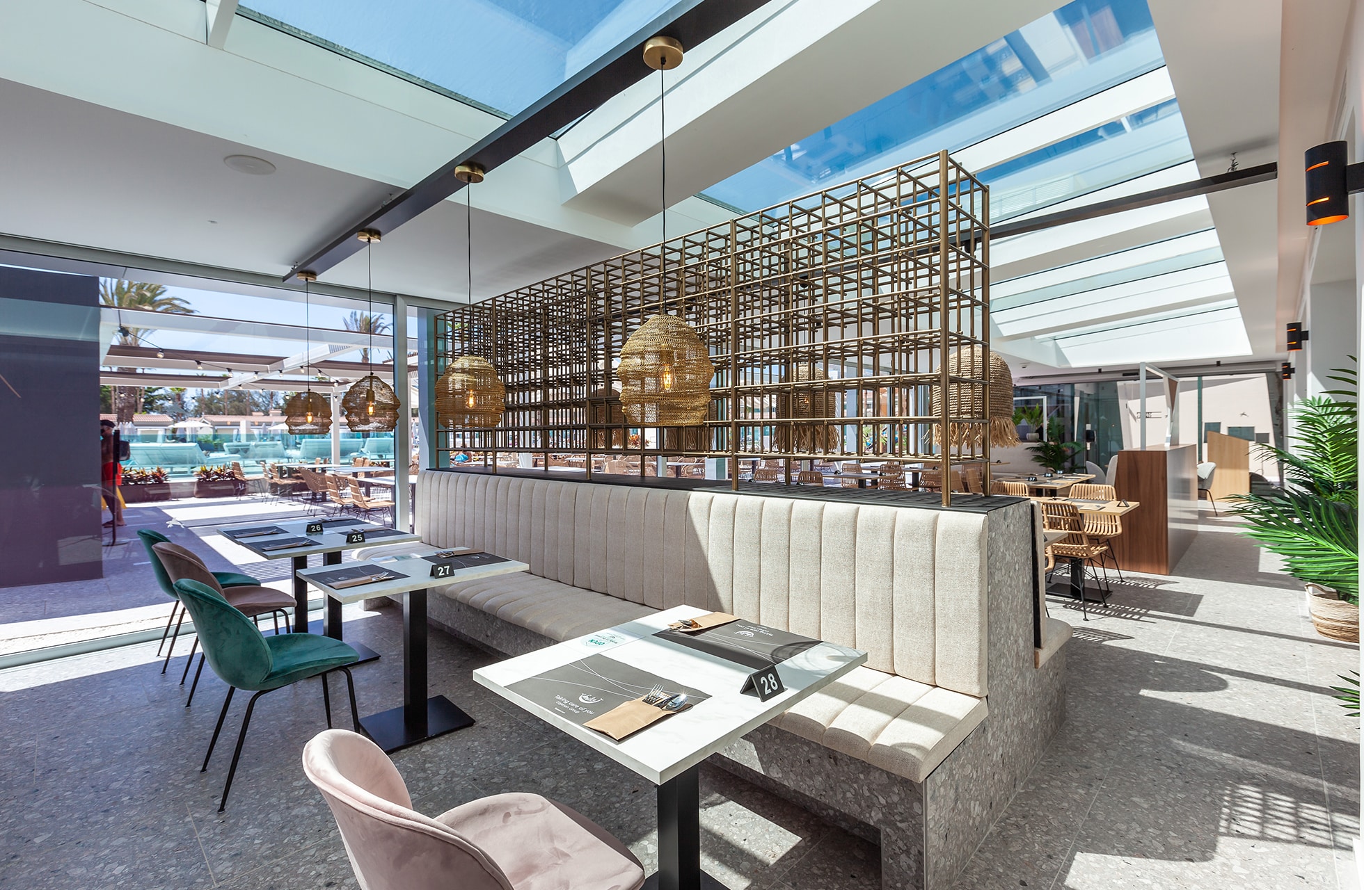 lys og moderne hotellrestaurant med båser, dekkede bord, dekorative lamper og åpent tak med utsikt mot bassengområde i dagslys
