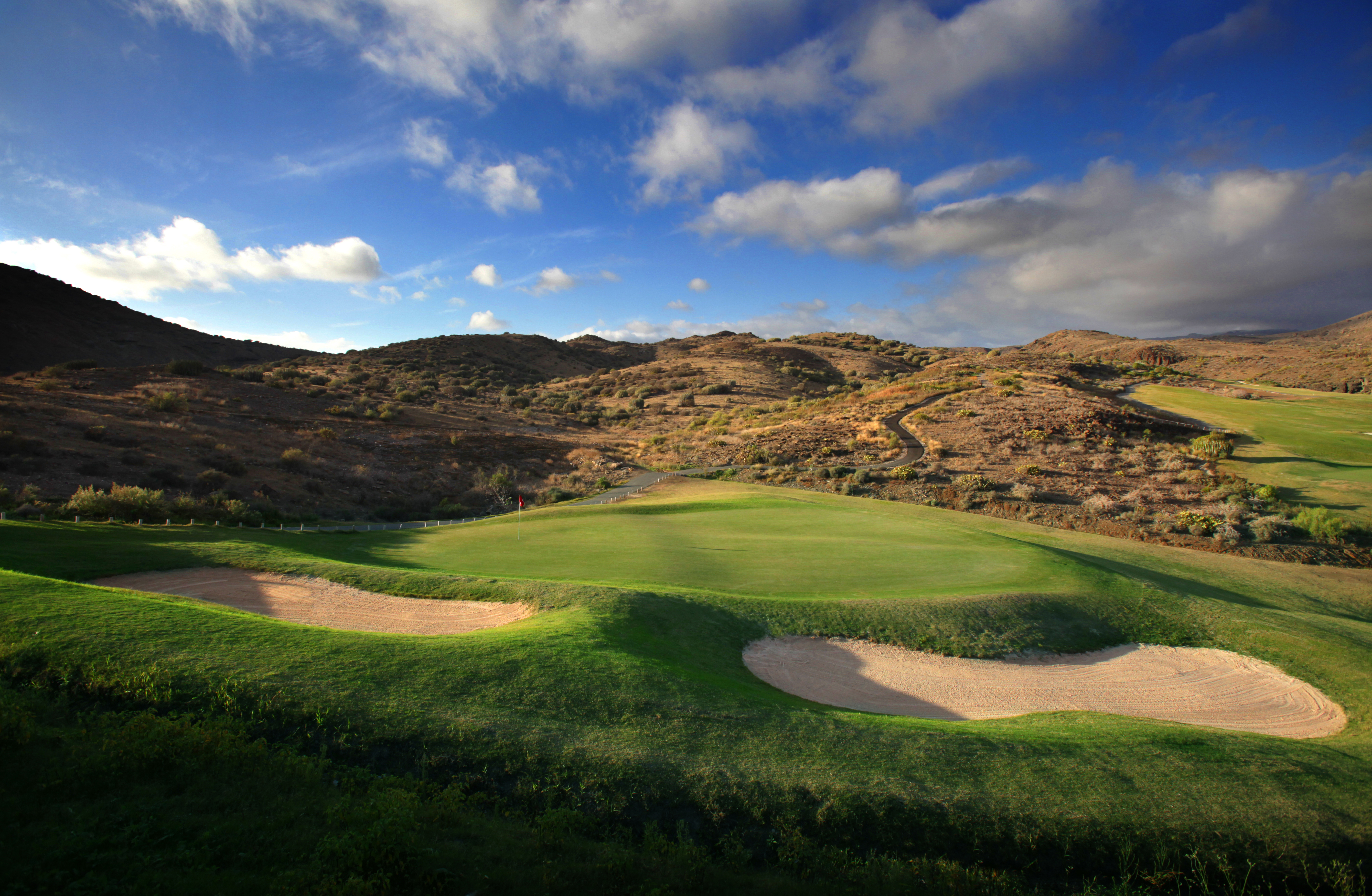 golfviheriö salobre new course -kentällä, kaksi bunkkeria avoimessa ja kumpuilevassa maisemassa, vihreät väylät ja vuoret taustalla päivänvalossa
