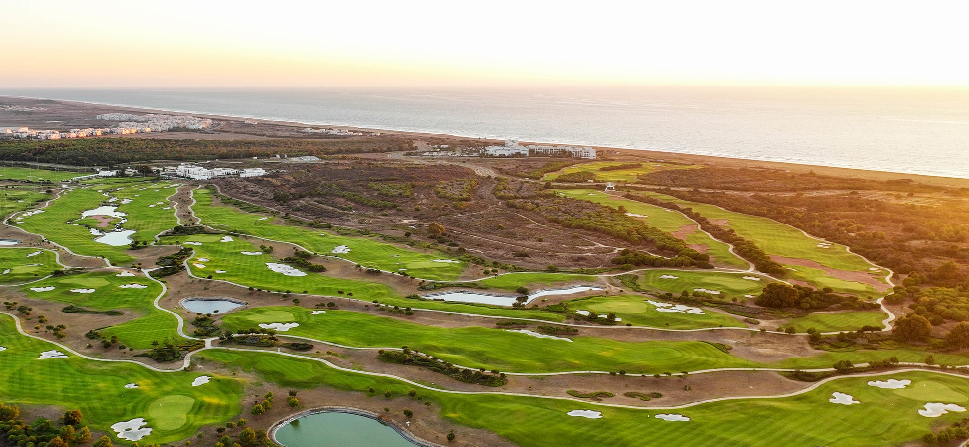 Bred luftfoto over banen med vandhazarder og bunkers ved havet.
