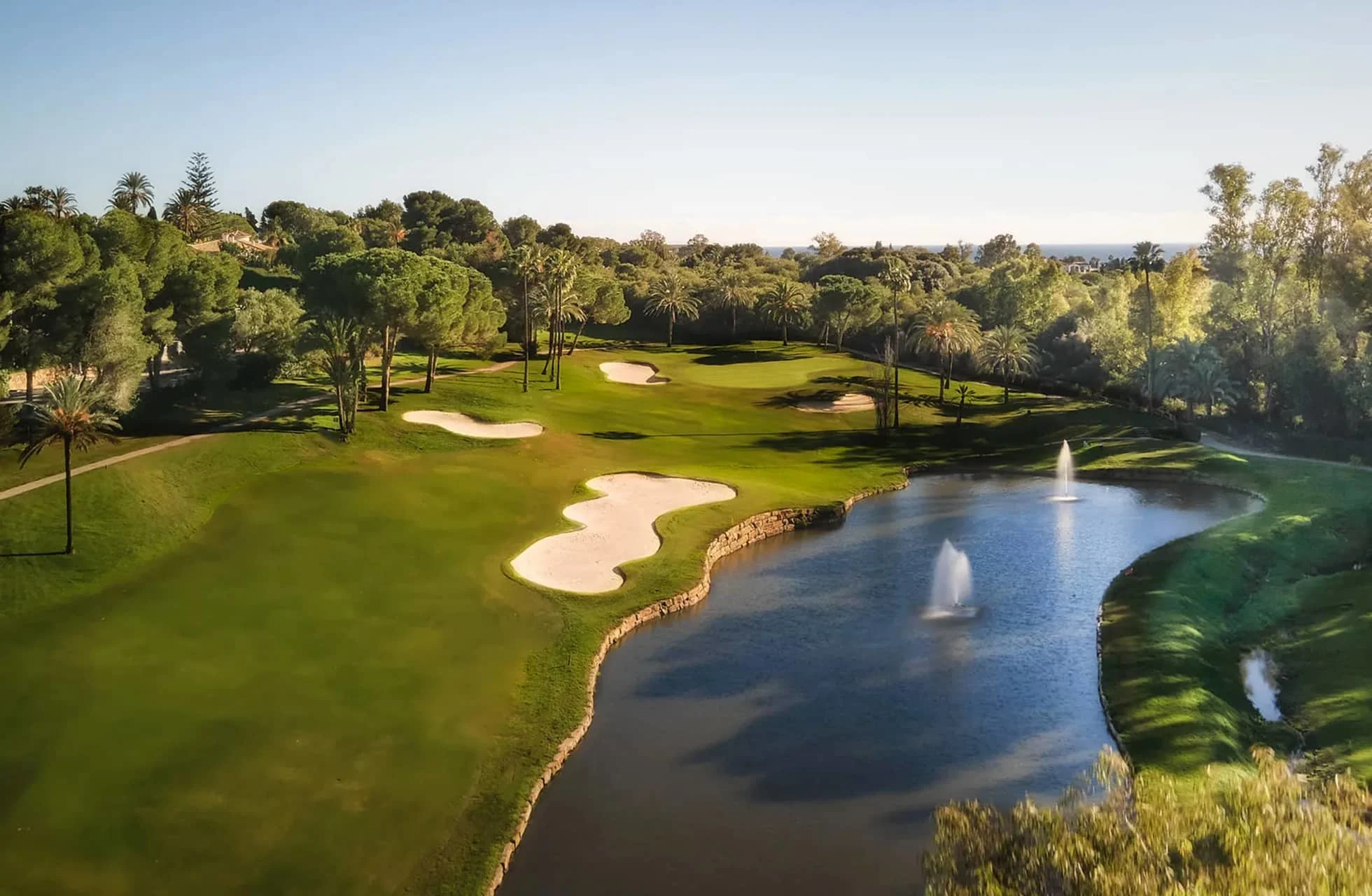 flyfoto av el paraiso golf med green og fairway ved stort vannhinder med fontene, omgitt av bunkere og trær i varmt dagslys